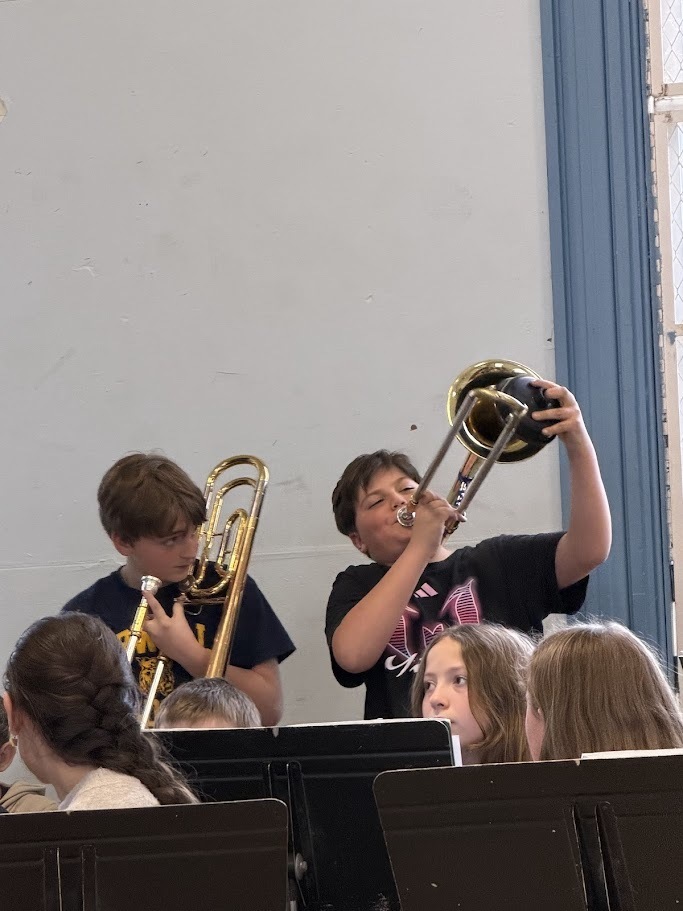 Two students play brass instruments, including a trombone, during a school band performance.