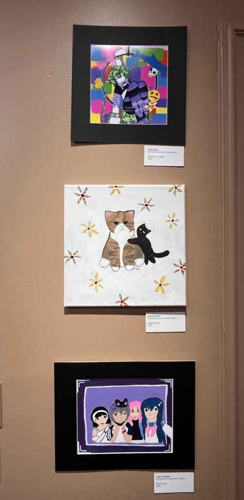 Vertical display of three framed student artworks, including colorful abstract art, a painting of two cats, and an anime-style portrait.