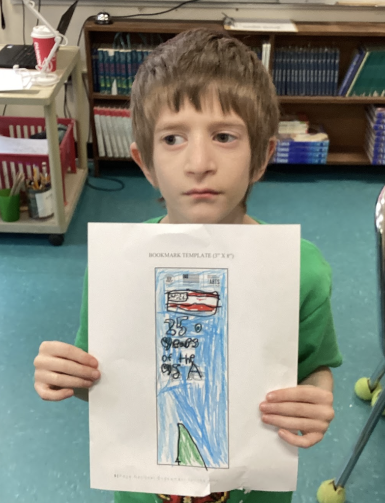 Student holds a bookmark design reading “250 anniversary” with a Statue of Liberty drawing.