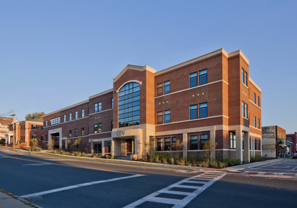 Exterior view of the Community College of Vermont campus in Rutland, showing a large red-brick academic building with tall windows at a street corner on a clear day.
