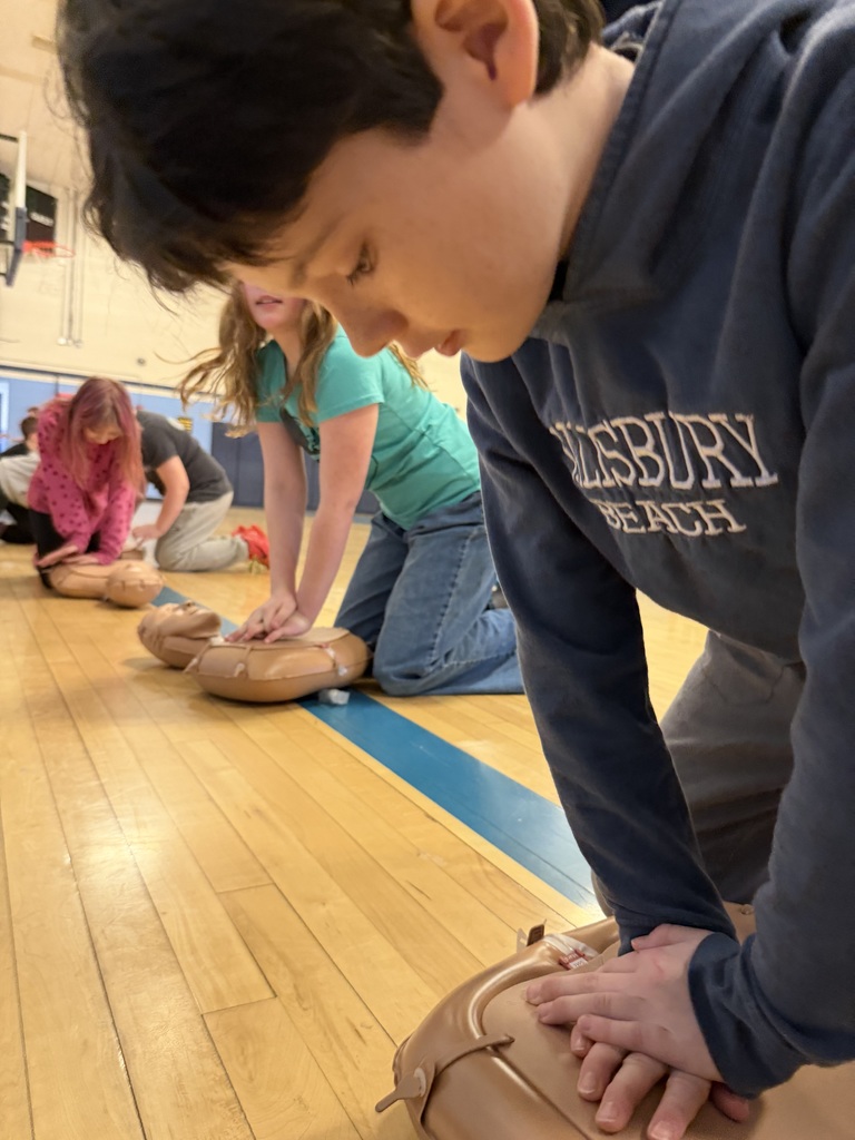Close-up of a student performing chest compressions on a CPR mannequin while classmates practice in the background.