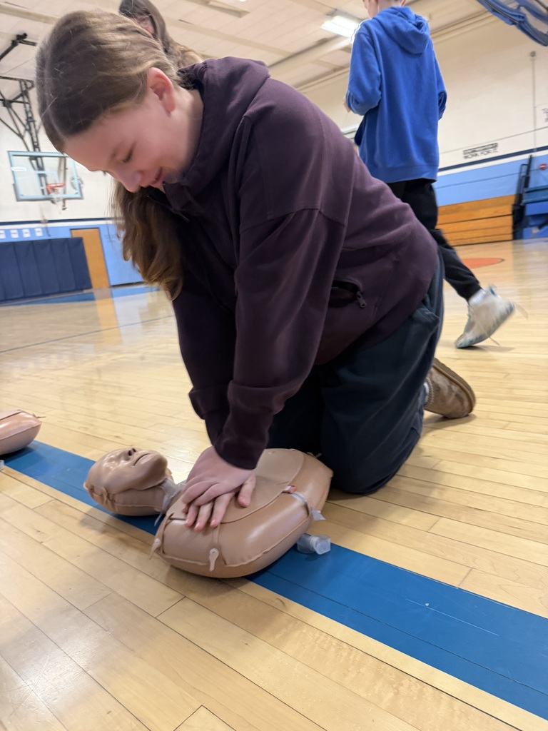 Student practices chest compressions on a CPR mannequin during hands-on emergency response training in the school gym.