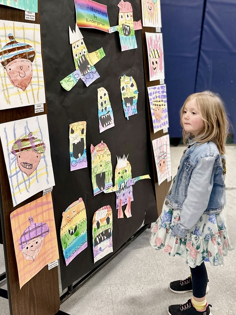 A young student looks closely at a display board of colorful kindergarten “Color Monster” drawings.