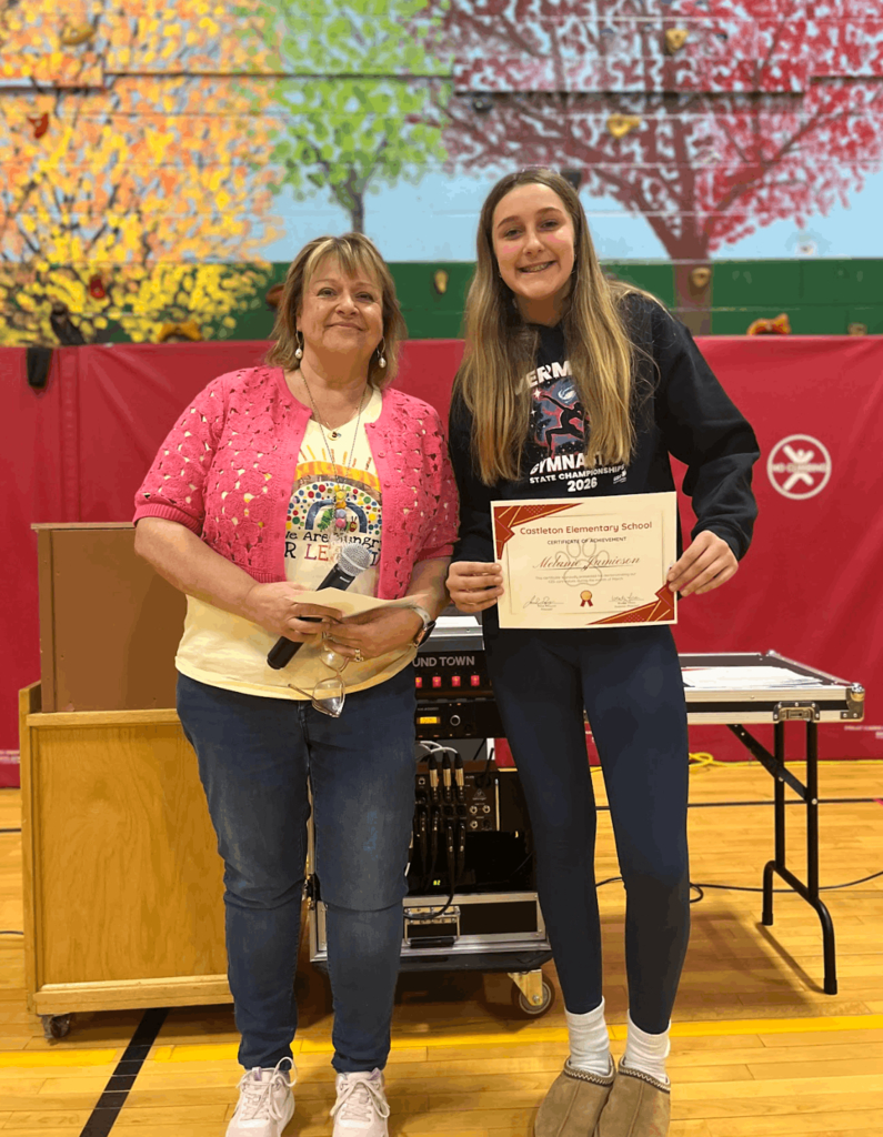 Staff member stands with a student holding a certificate, smiling for a photo during an awards presentation.