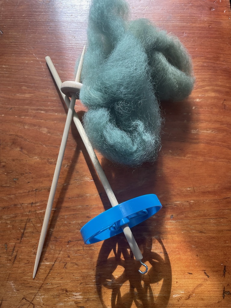 Close-up of wool roving and two drop spindles resting on a wooden table, used for spinning yarn.