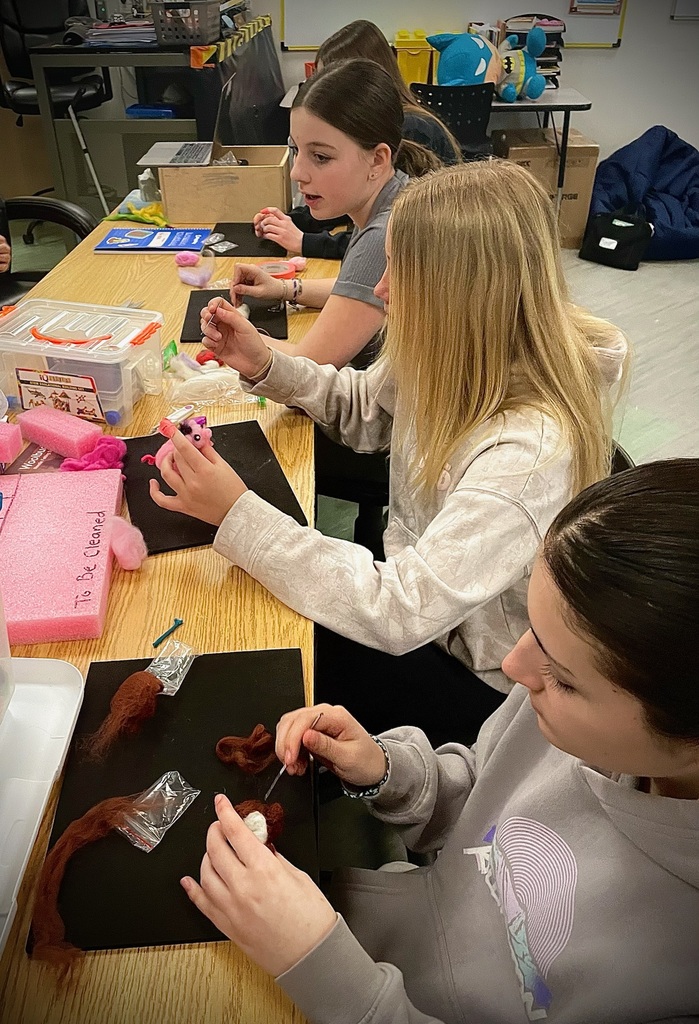 Group of students using felting needles to shape wool into small figures while seated around a classroom table.