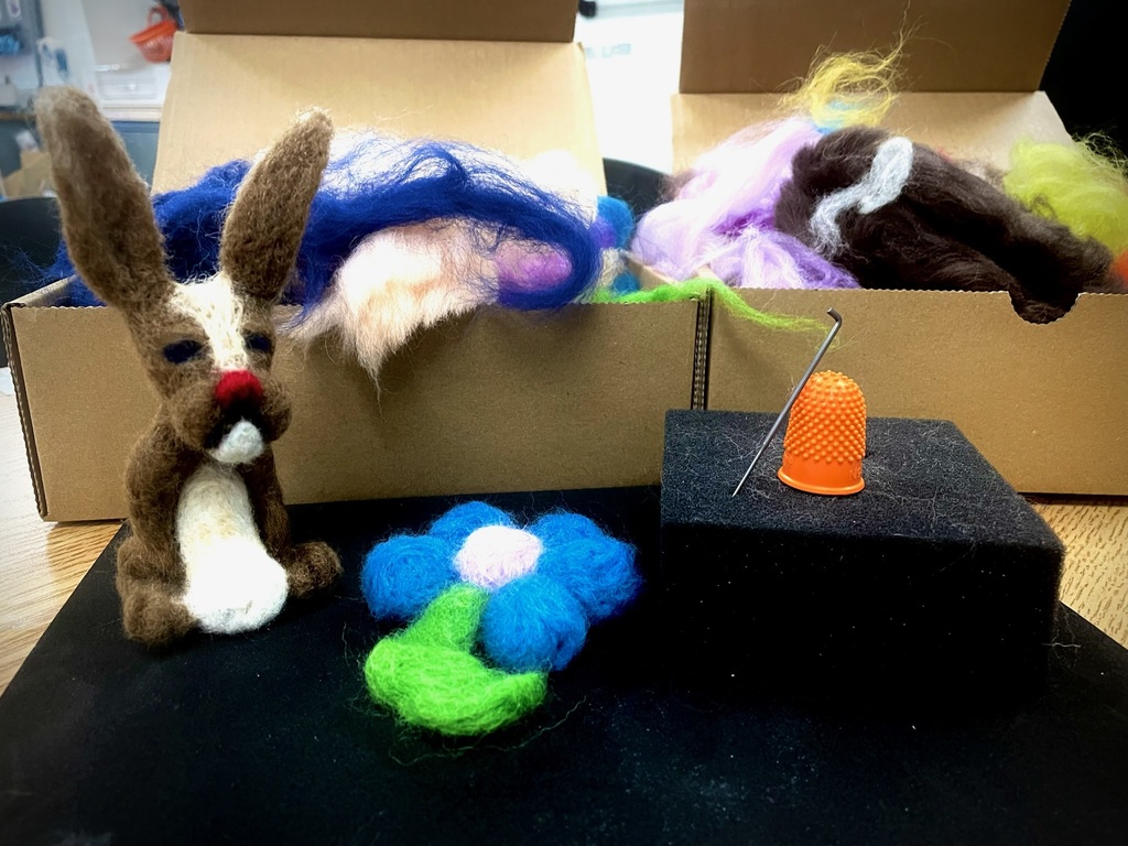 Finished needle-felted creations, including a small animal figure and a flower, displayed with wool and felting tools.