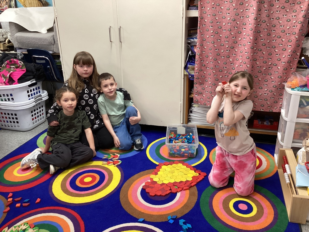 Four students sit on a colorful rug working together to create a heart-shaped design using pattern blocks.