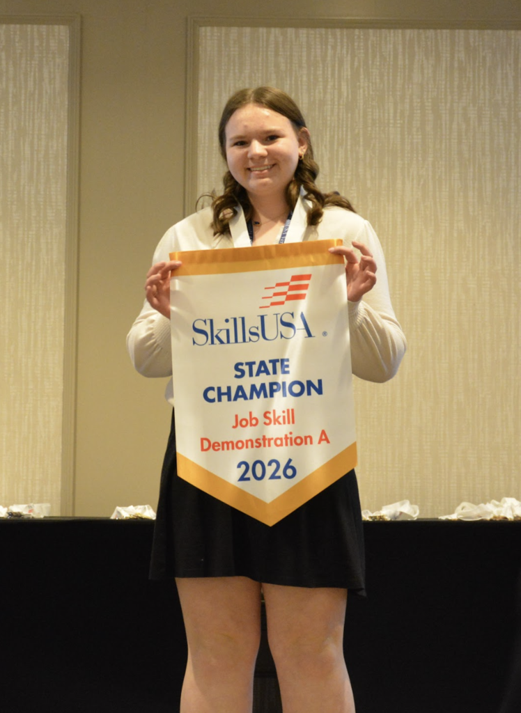 A student smiles while holding a SkillsUSA banner that reads “State Champion Job Skill Demonstration A 2026,” wearing a medal around their neck.