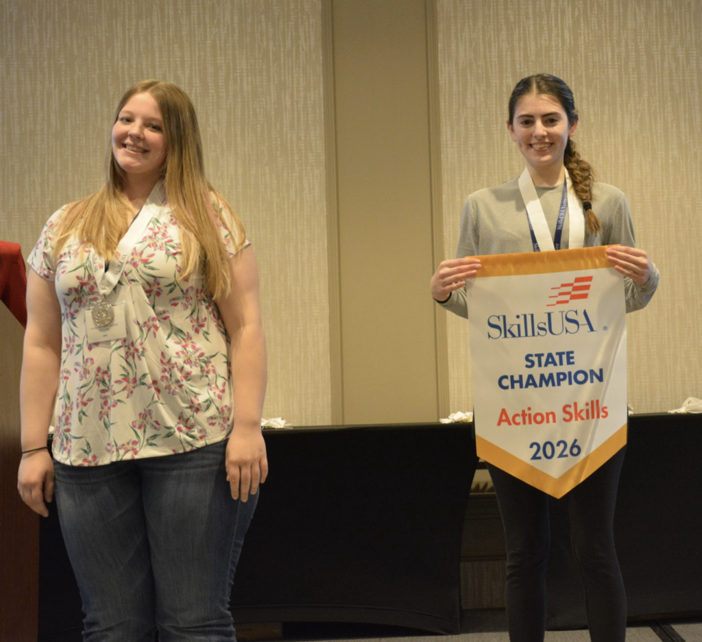 Two students stand together; one wears a medal and the other holds a SkillsUSA banner reading “State Champion Action Skills 2026.”
