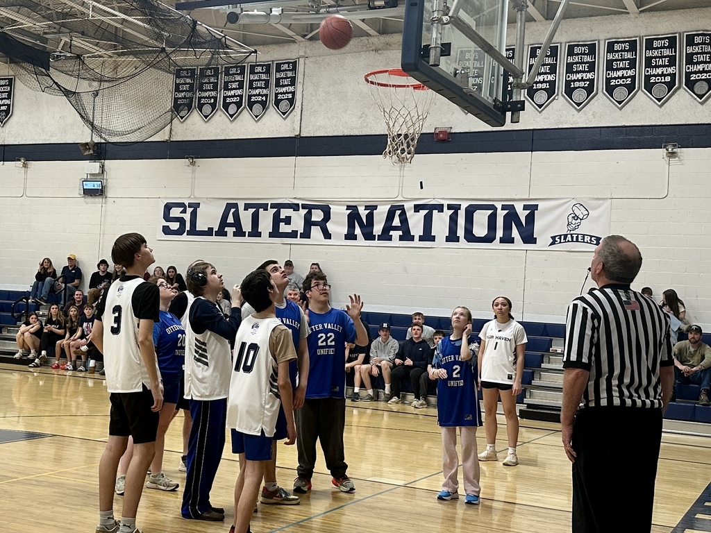 Players from both teams look up at the hoop as the basketball descends toward the rim during a Unified Basketball game.