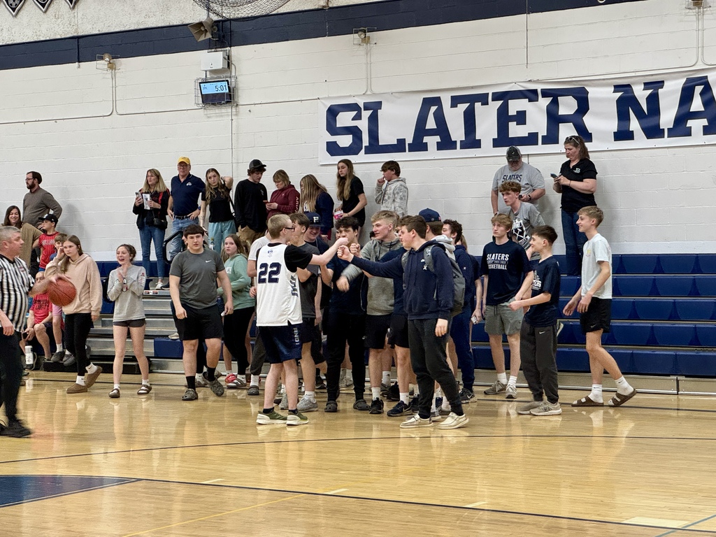 Students on the sidelines cheer and celebrate together, with two players exchanging a fist bump.