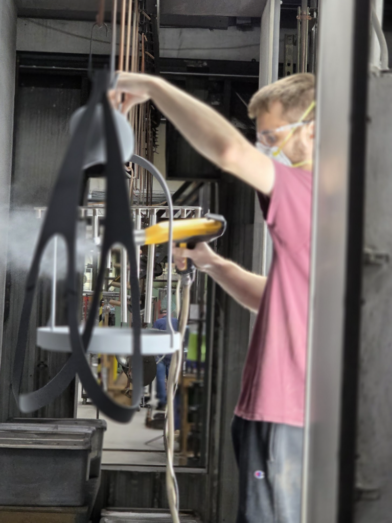 A worker wearing safety glasses operates equipment while holding a metal frame, demonstrating part of the production process.