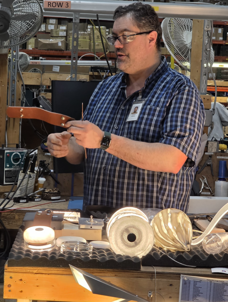 An employee demonstrates lighting components at a workstation, showing different lamp designs and materials.