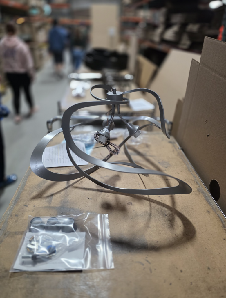 Close-up of a partially assembled metal light fixture resting on a workbench with small parts and hardware nearby.