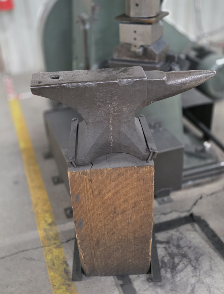 Close-up of a metal anvil mounted on a wooden base in an industrial workshop setting.
