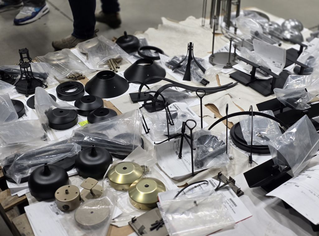 A table filled with various metal lighting parts and components organized in bags and grouped by type.
