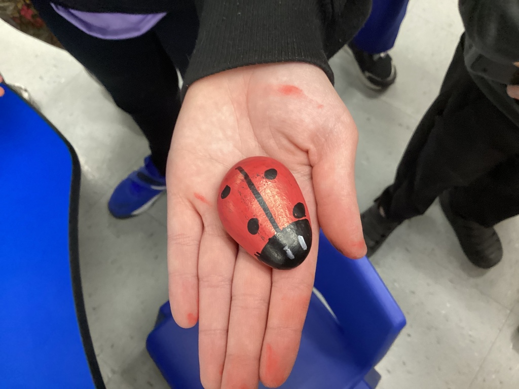 Close-up of a hand holding a painted rock designed as a red and black ladybug.