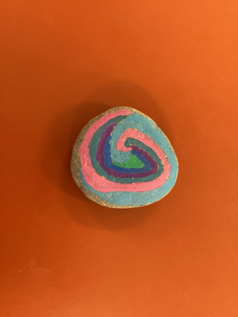 Small painted rock on an orange table featuring a spiral design in pink, blue, green, and purple.