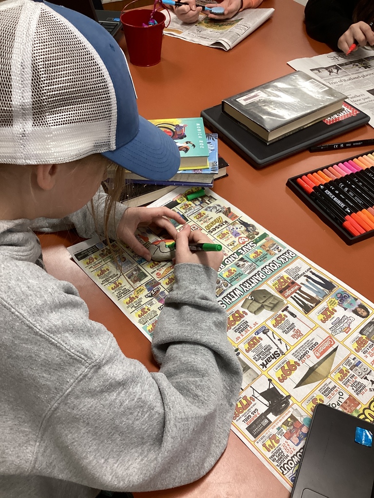 Student wearing a cap draws on a rock with a green marker while working over a newspaper-covered table.