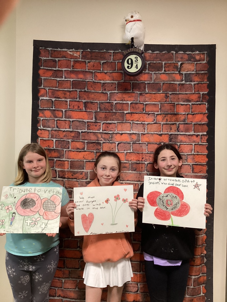 Three students hold detailed poppy posters featuring messages about honoring veterans and those who served.