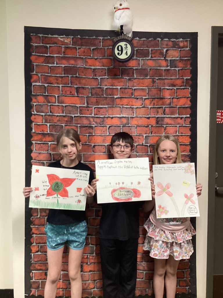 Three students hold posters with poppy illustrations and messages recognizing fallen soldiers and veterans.