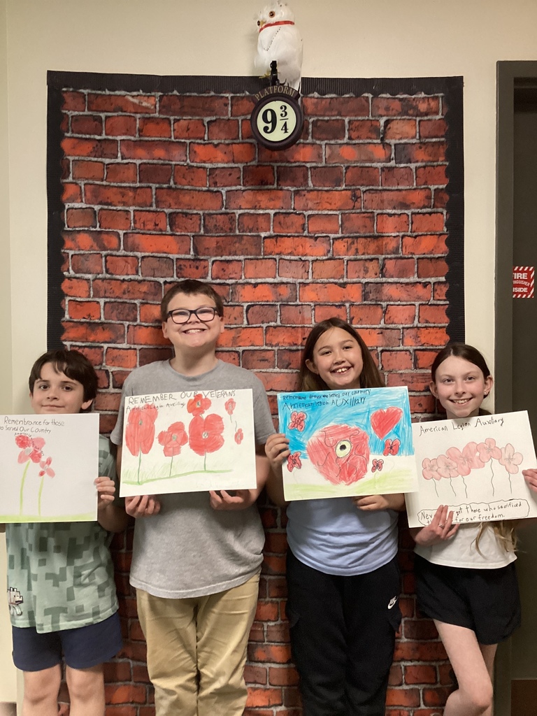 Four students smile while holding colorful poppy artwork with messages about remembering veterans.
