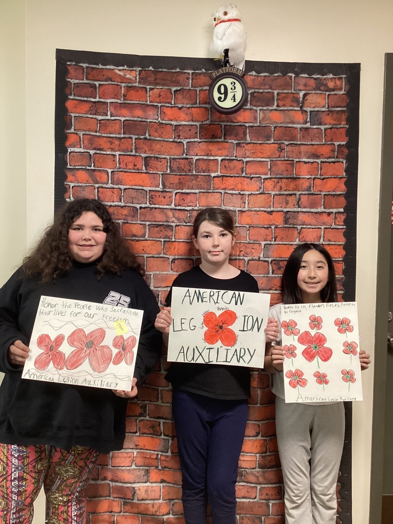 Three students present poppy artwork with bright red flowers and “American Legion Auxiliary” written on the posters.