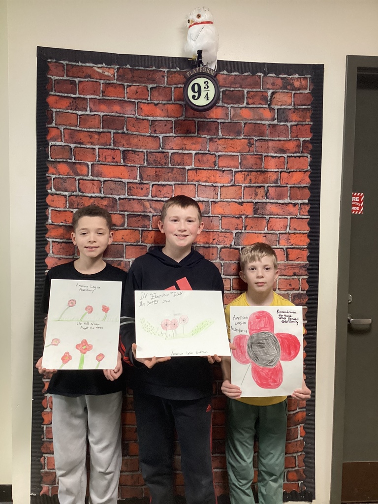 Three students stand side by side holding poppy drawings with red flowers and handwritten messages of remembrance.