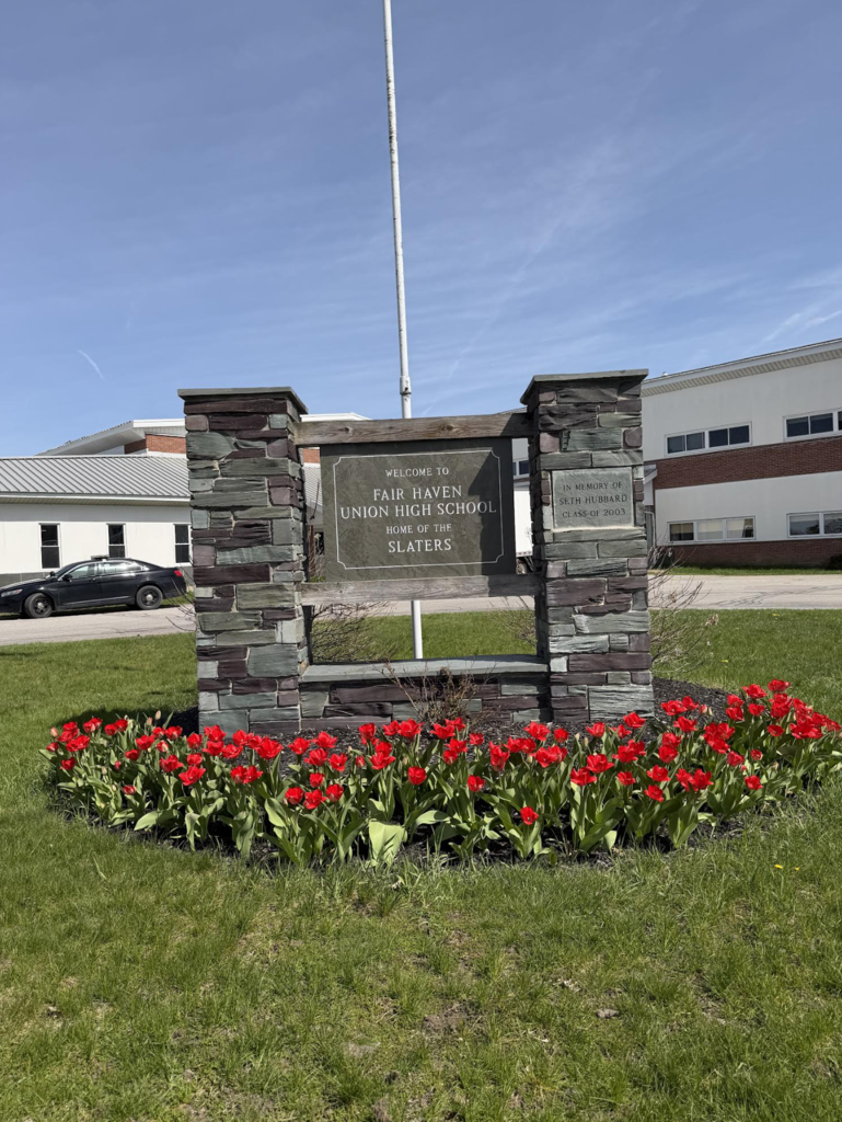 A stone sign reading “Welcome to Fair Haven Union High School, Home of the Slaters” is surrounded by blooming red tulips in a landscaped bed in front of the school.