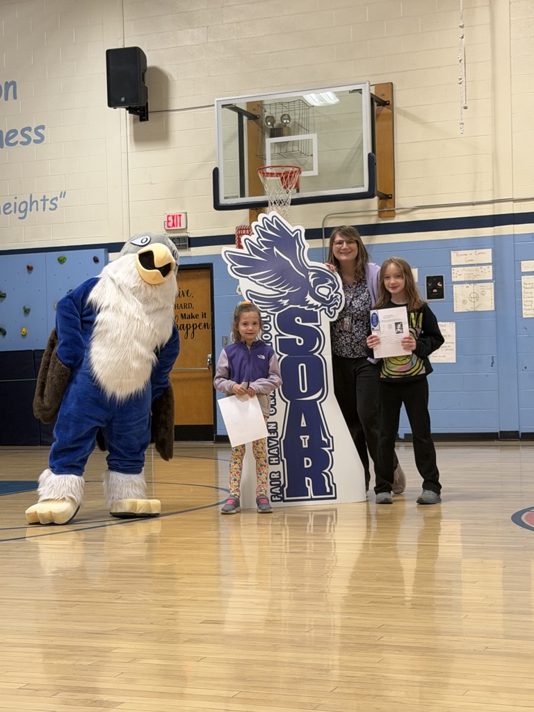 Two students holding certificates and one adult posing with a blue eagle mascot in a gymnasium in front of a "SOAR" sign.