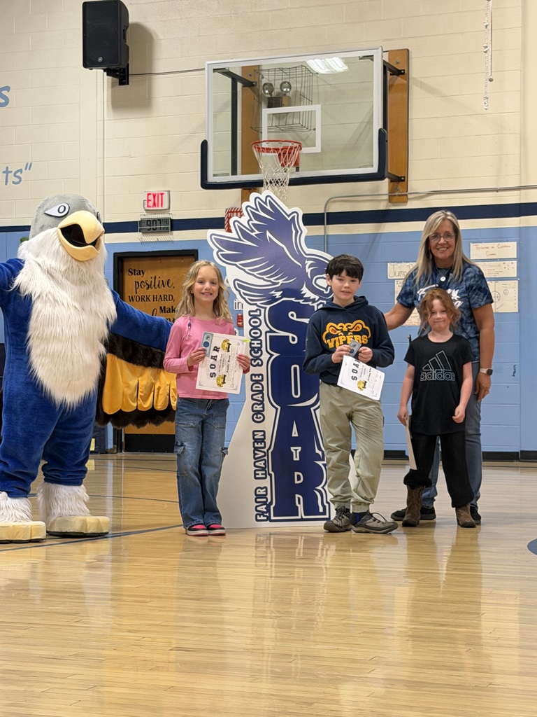 Three students holding certificates and an adult woman pose with a blue eagle mascot in a school gymnasium in front of a "SOAR" sign.