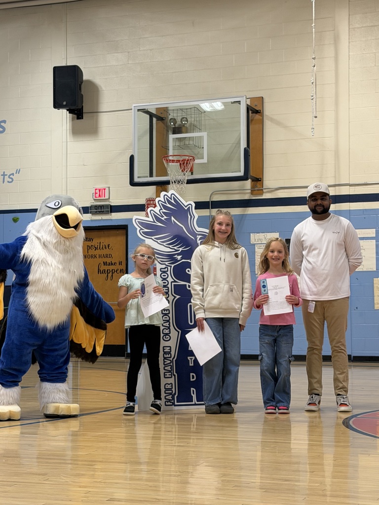 Three students holding certificates and one adult posing with a blue eagle mascot in a gymnasium in front of a "SOAR" sign.