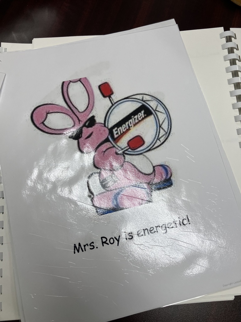  A page from a tribute book featuring a colorful drawing of the Energizer Bunny wearing sunglasses and beating a drum. Below the illustration, the typed text reads, "Mrs. Roy is energetic!" The page is protected by a plastic sheet.  