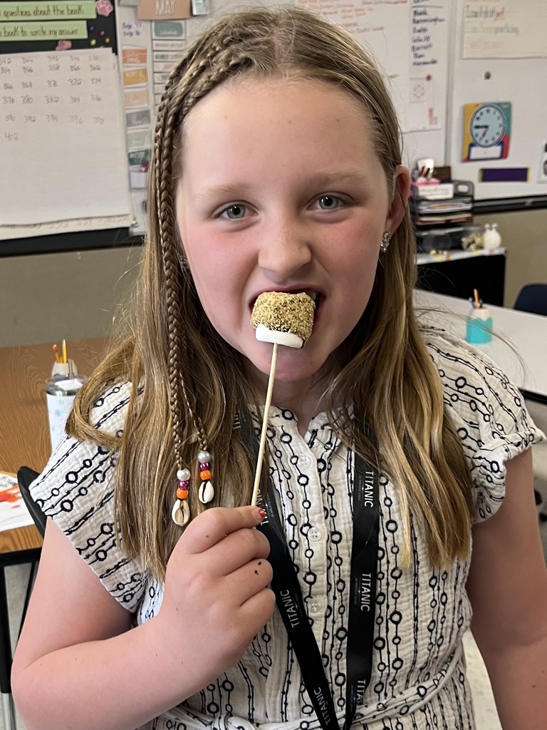  A young girl with braided hair and a "Titanic" lanyard taking a bite of a marshmallow treat covered in graham cracker crumbs.  IMG_5638.jpg: A young boy wearing a green t-shirt with a dinosaur print taking a bite of a s'more on a stick.