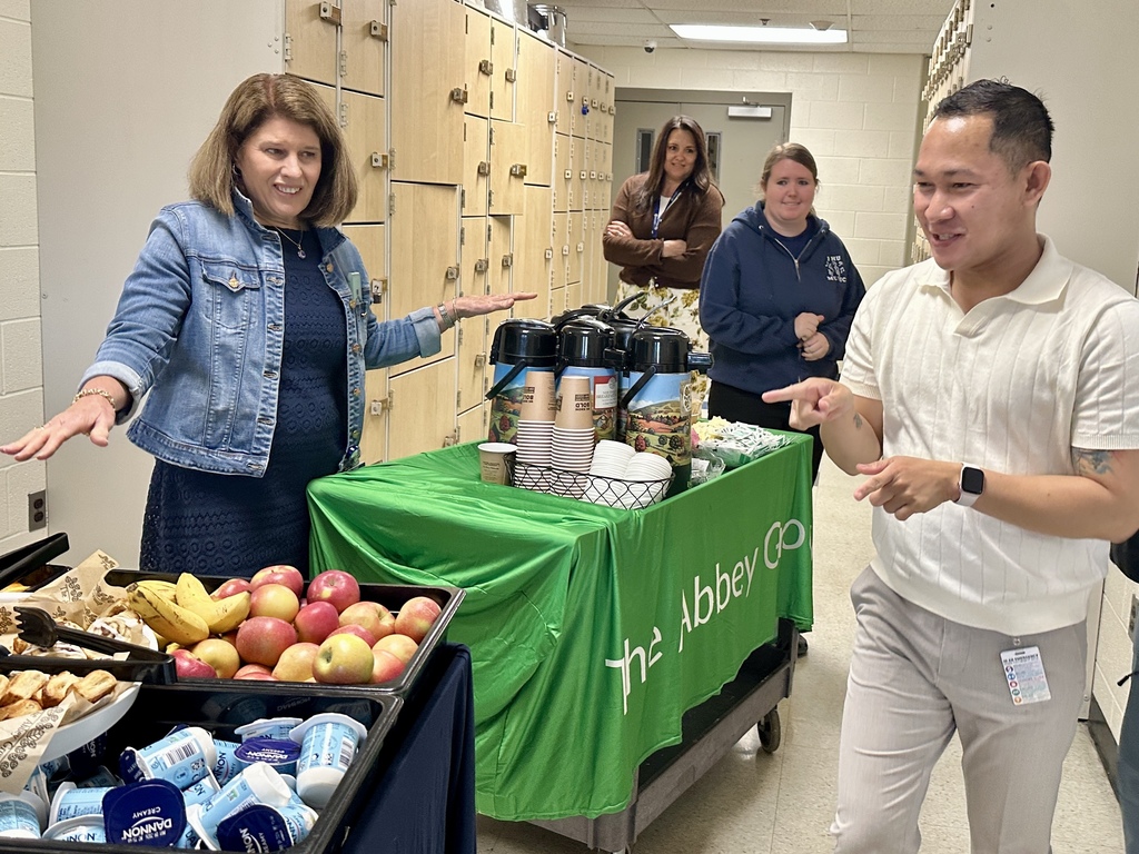 Staff gather around a mobile coffee and snack station in a hallway, smiling and chatting while preparing drinks.
