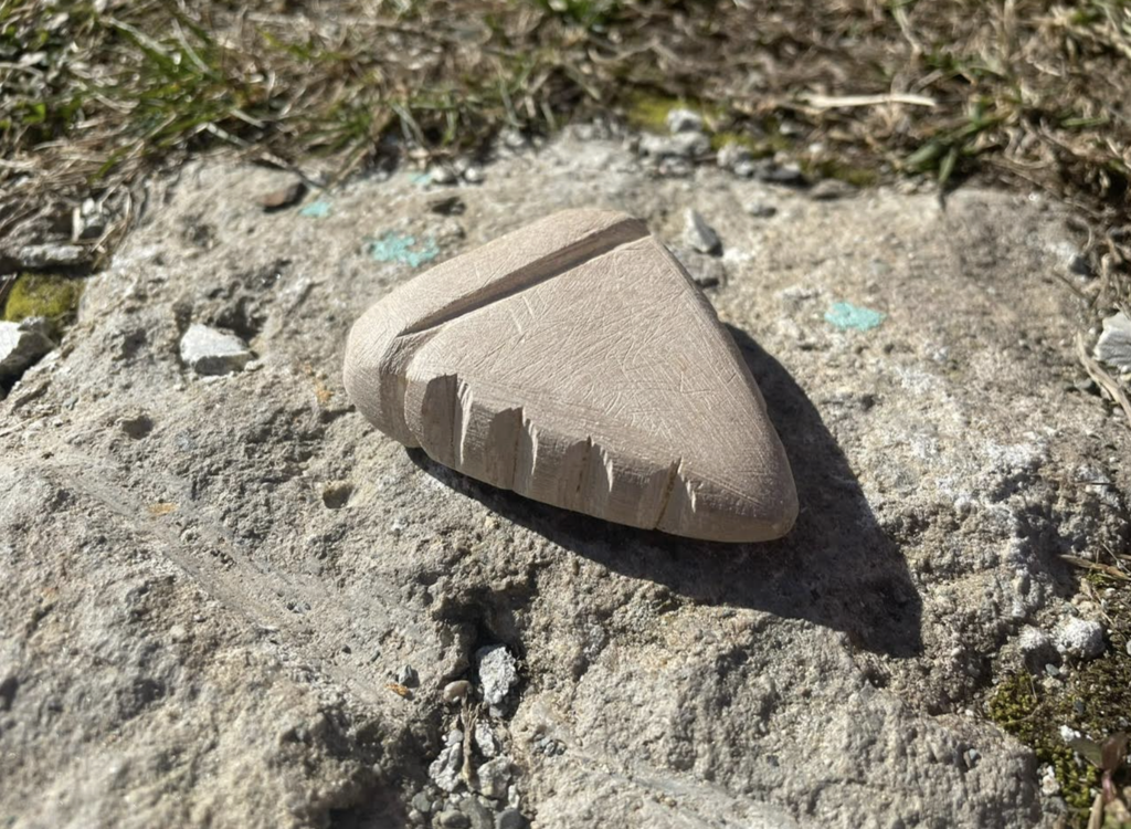 A partially carved soapstone piece resting on a rough outdoor surface, showing fresh tool marks and shaping in progress under bright sunlight.