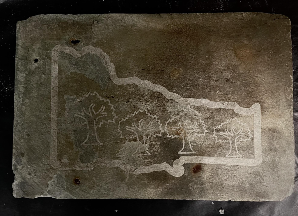 A slate tile engraved with the outline of the state of Vermont and several trees inside the shape, creating a nature-themed design.