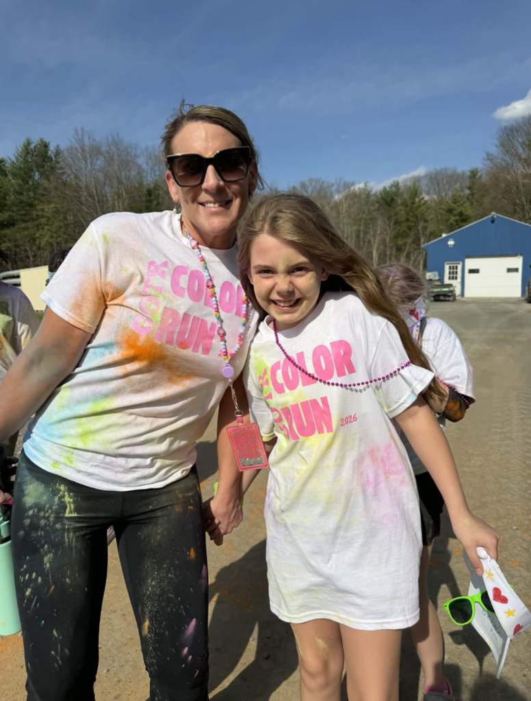 An adult volunteer and a Girls on the Run participant smile together while covered in colorful powder after completing the practice Color Run.