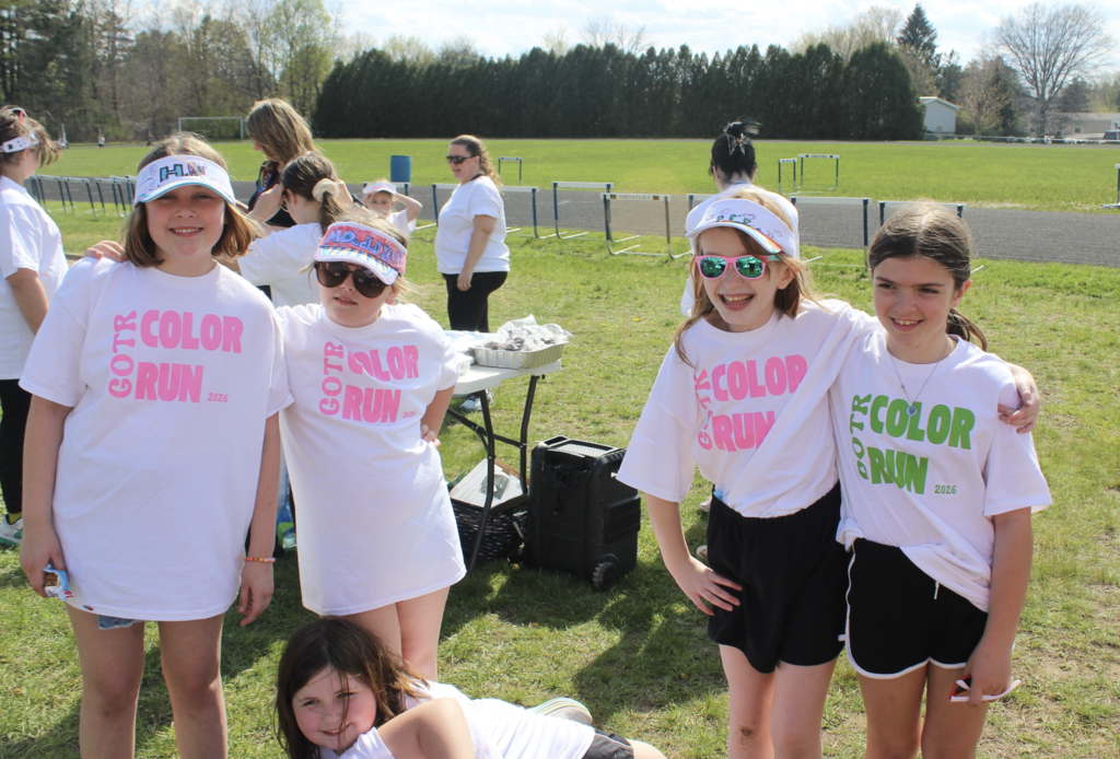 Four Girls on the Run participants stand together outdoors smiling in white Color Run shirts and decorated visors during the practice 5K event.