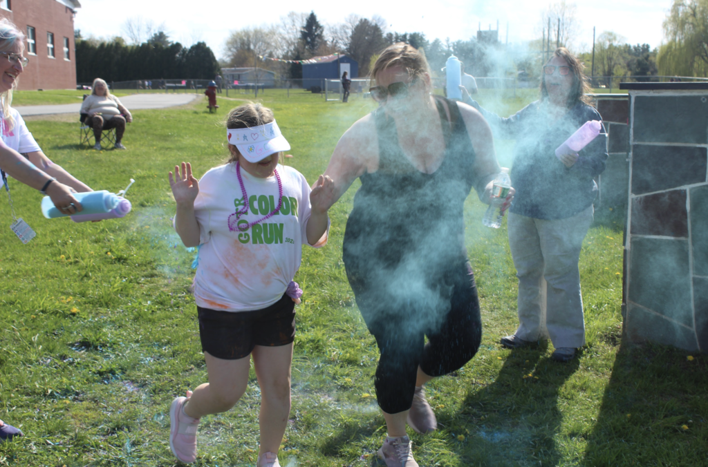 A Girls on the Run participant runs through a cloud of blue powder while adult volunteers toss color during the practice Color Run.