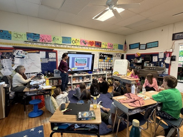 Students relax on chairs, beanbags, and stools in a classroom while listening attentively to a guest speaker leading a group discussion.