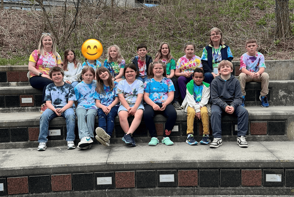 A group of students and teachers wearing tie-dyed shirts pose together for a group photo during their Montshire Museum field trip.