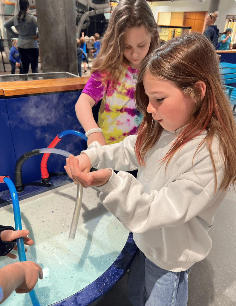 Two students experiment with a foam fountain exhibit at the Montshire Museum while steam and bubbles rise from tubes in front of them.