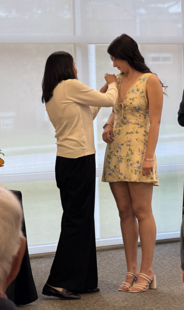 A mentor teacher pins a student teacher wearing a yellow floral dress during the Vermont State University student teaching pinning ceremony.