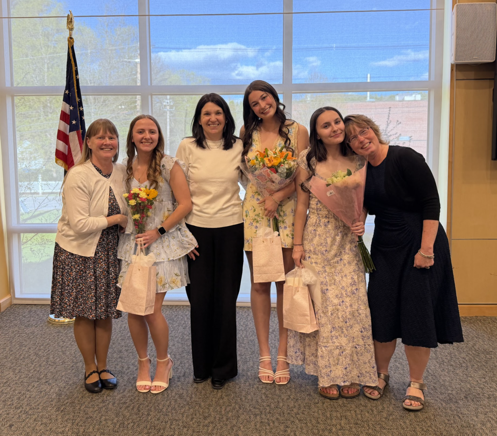 Three mentor teachers and three student teachers stand together smiling during the student teaching pinning ceremony at Vermont State University. The student teachers hold flowers and gift bags.