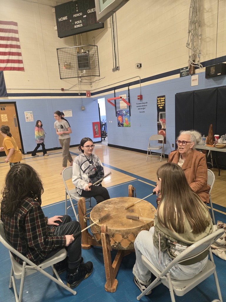 Students sit around a large traditional drum with Miss Lucy Neel in the school gym as they learn about drumming and Abenaki culture.