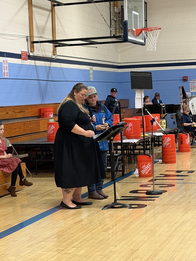 A student stands beside Mrs. Hutchins at a microphone while receiving recognition during the FHGS spring concert.