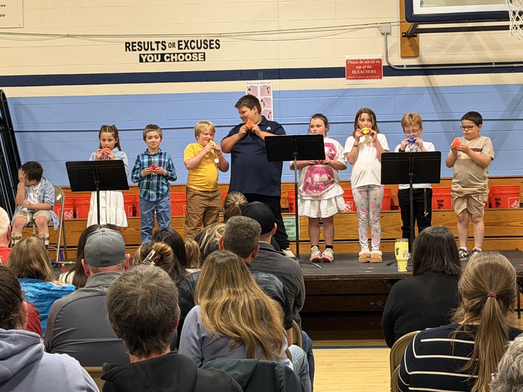 Elementary students stand on stage in the gym playing colorful ocarinas during the FHGS spring concert while families watch from the audience.