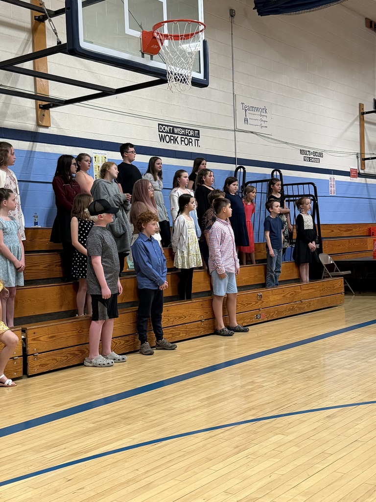 A choir of FHGS students stands on risers in the gym preparing to sing during the spring concert performance.